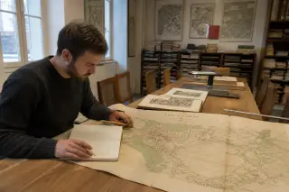 Archival reading room with person studying an antique city map, surrounded by shelves of historical documents and soft morning light.