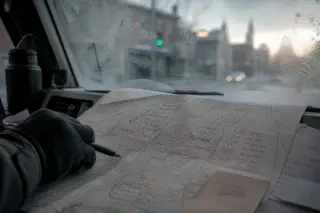 Detail of a courier’s gloved hand hovering over a hand-annotated city map on a van dashboard, misty morning light, suggesting thoughtful route planning.