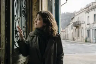 Woman tracing ironwork on old villa doorway in soft morning light, blurred empty street behind