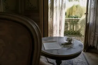 Vintage letter and tea set on a marble table in a quietly sunlit Belle Époque villa parlor, with an open window and blurred thermal garden outside