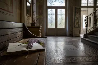 Lobby of a historic Bains-les-Bains villa with soft winter light, an old bench, open guestbook, and a wisteria sprig, in a contemplative, tranquil atmosphere.