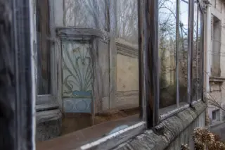 Oblique view through an old veranda window showing vintage tile and woodwork details of a villa façade, with condensation and soft winter light.