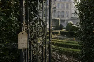 aged iron gate with intricate initials partially open to reveal overgrown garden and historic hotel facade in soft winter morning light, archival tag tied to gate