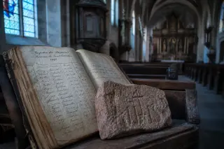 Old parish ledger and stone fragment on church pew, bathed in soft bluish daylight with blurred nave in the background