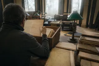 Researcher examining old thermal spa documents by natural winter light in a Belle Époque archive