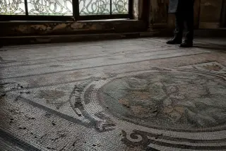Worn mosaic floor in a historic thermal lobby under soft winter light, with a lone person observing a faded tile detail in quiet contemplation.