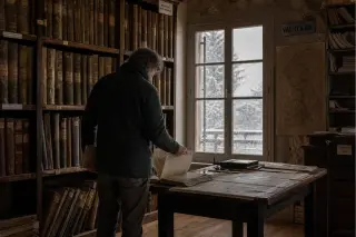 Man absorbed in studying old documents in a dusty archive room, with natural winter light and shelves of antique ledgers.