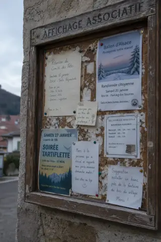 Close-up of an old community bulletin board covered with faded handwritten notes and flyers on a rough stone wall, illuminated by soft winter light in a quiet Vosges village.